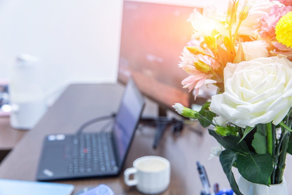 Flowers and laptop on table, empty office,light on flowers